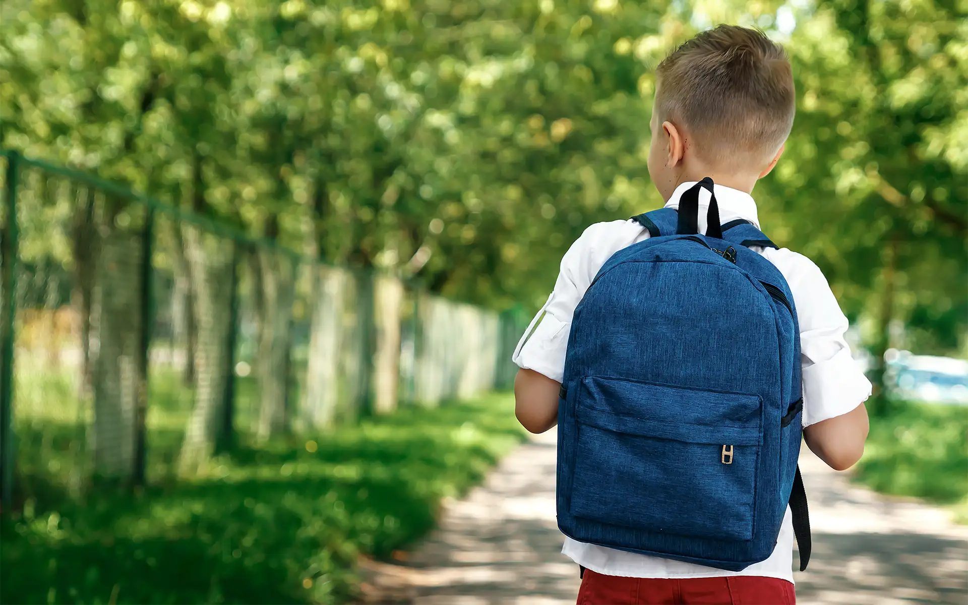 a rear view of an elementary-age boy on a street wearing a backpack