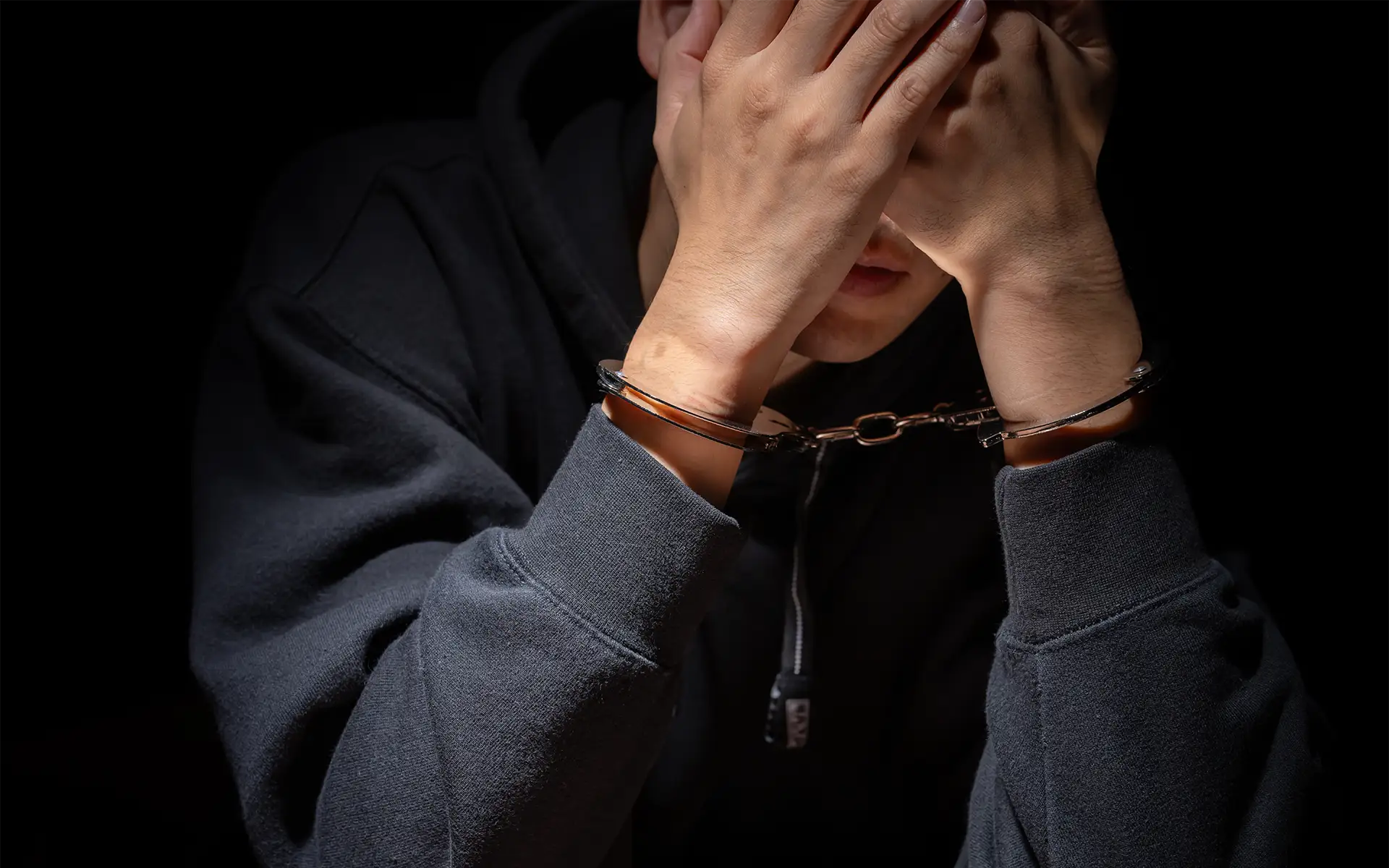 close-up of a man wearing handcuffs with his hands covering his face