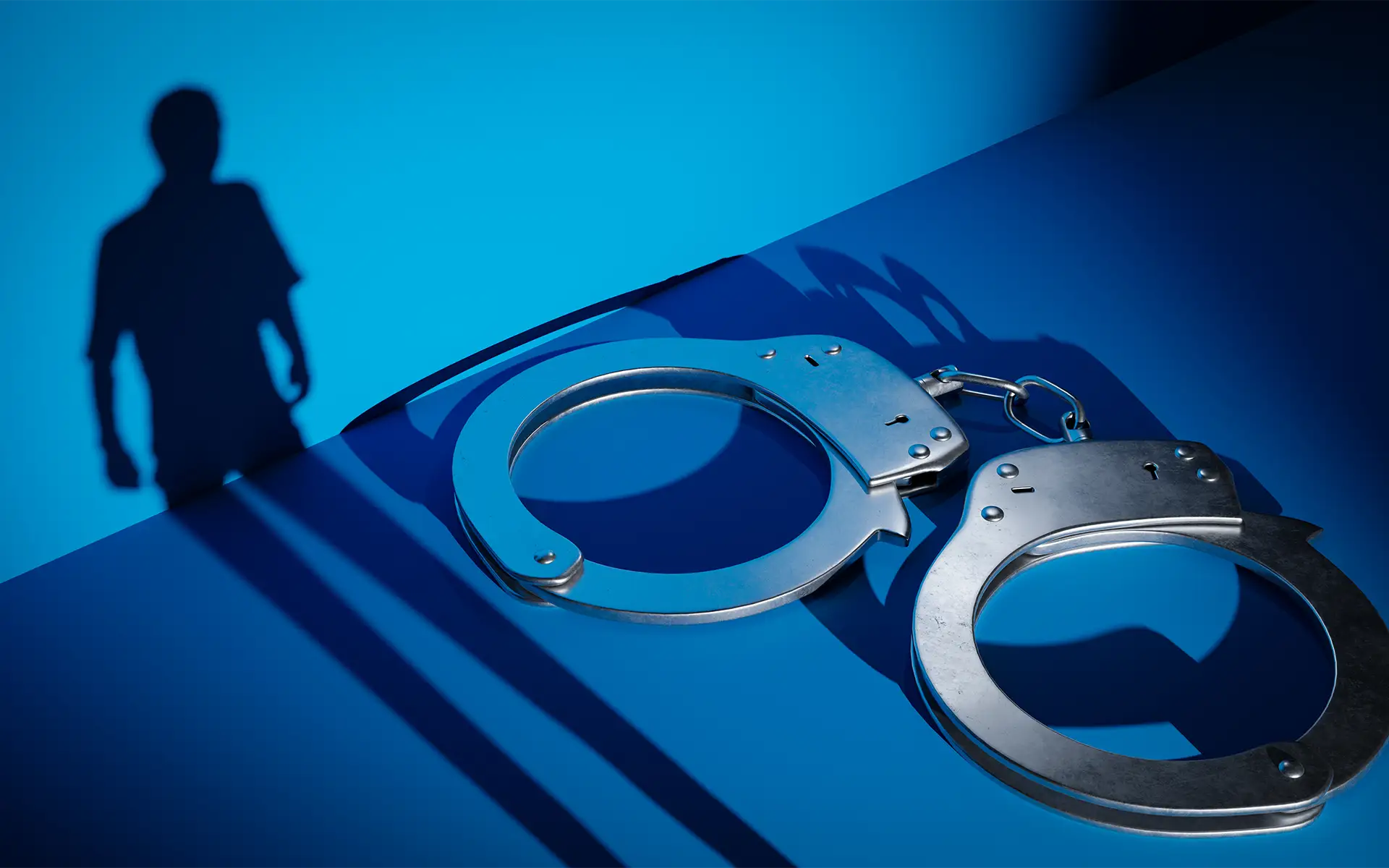 Handcuffs on a blue background with a shadow of a suspicious person looming next to the cuffs