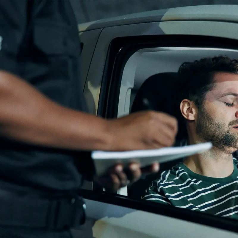 A man in a car at night handing a police officer his driver's license during a traffic stop