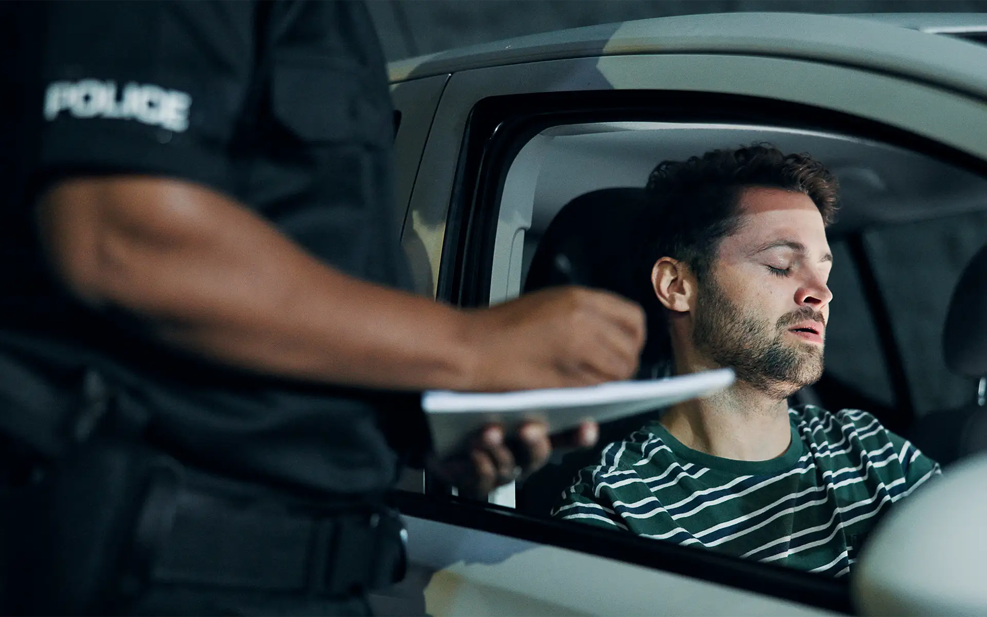 A man in a car at night handing a police officer his driver's license during a traffic stop